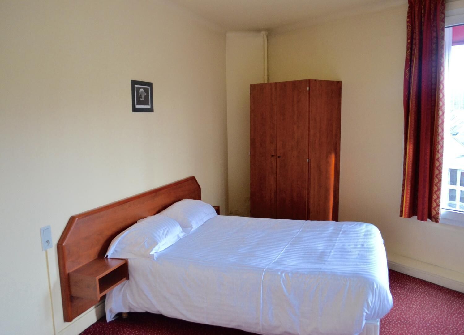 A bedroom with a single bed, a wooden wardrobe, and a small picture on the wall.