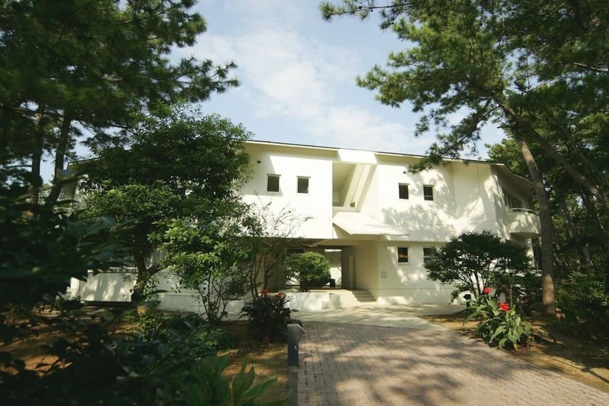 A two-story building with a flat roof, surrounded by trees and a paved driveway.