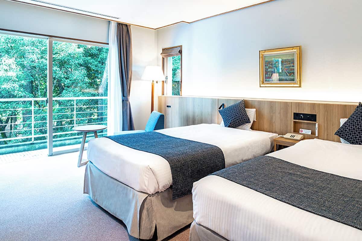 A hotel room with two beds, a large window, a desk, and a chair.