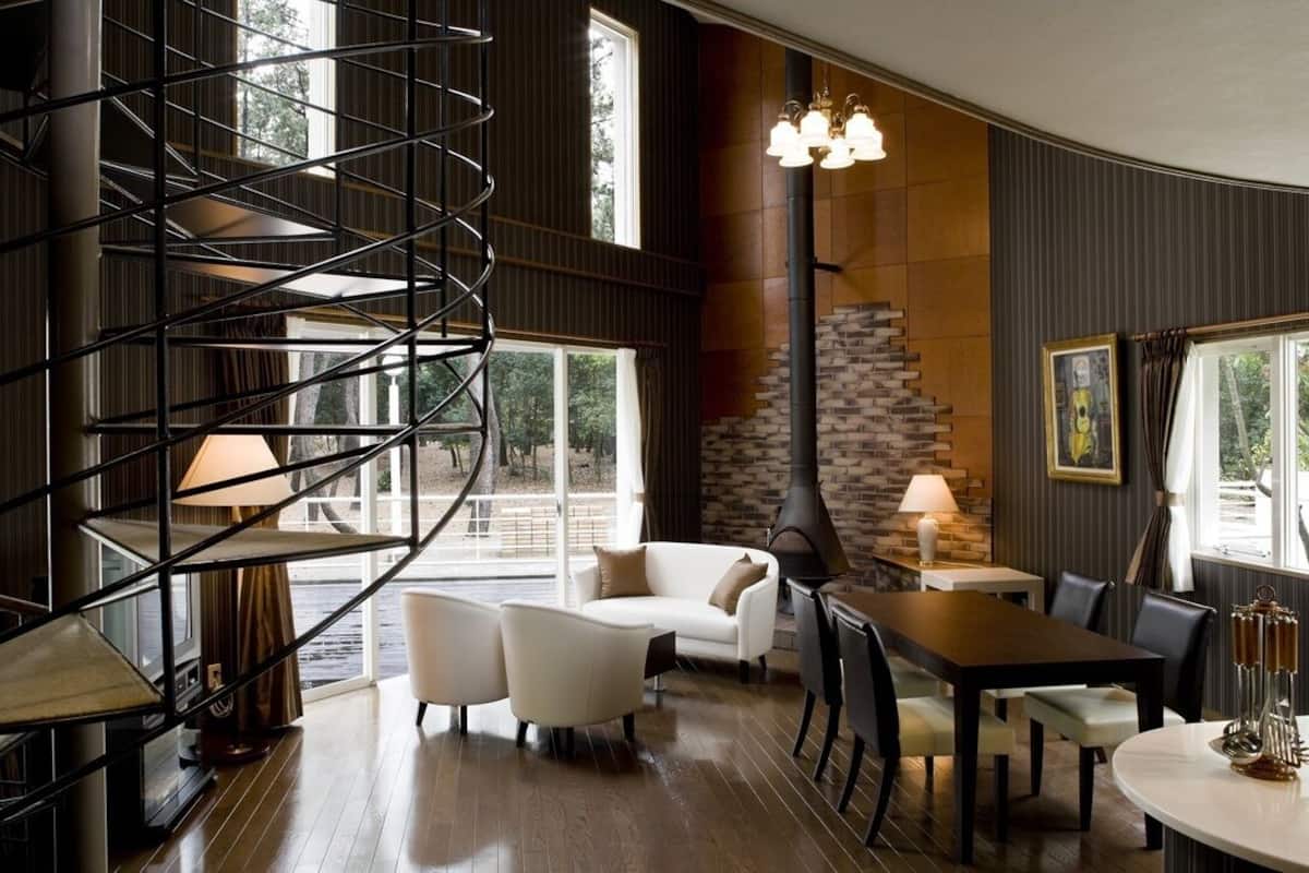A modern interior with a spiral staircase, a fireplace, a dining area, and large windows.