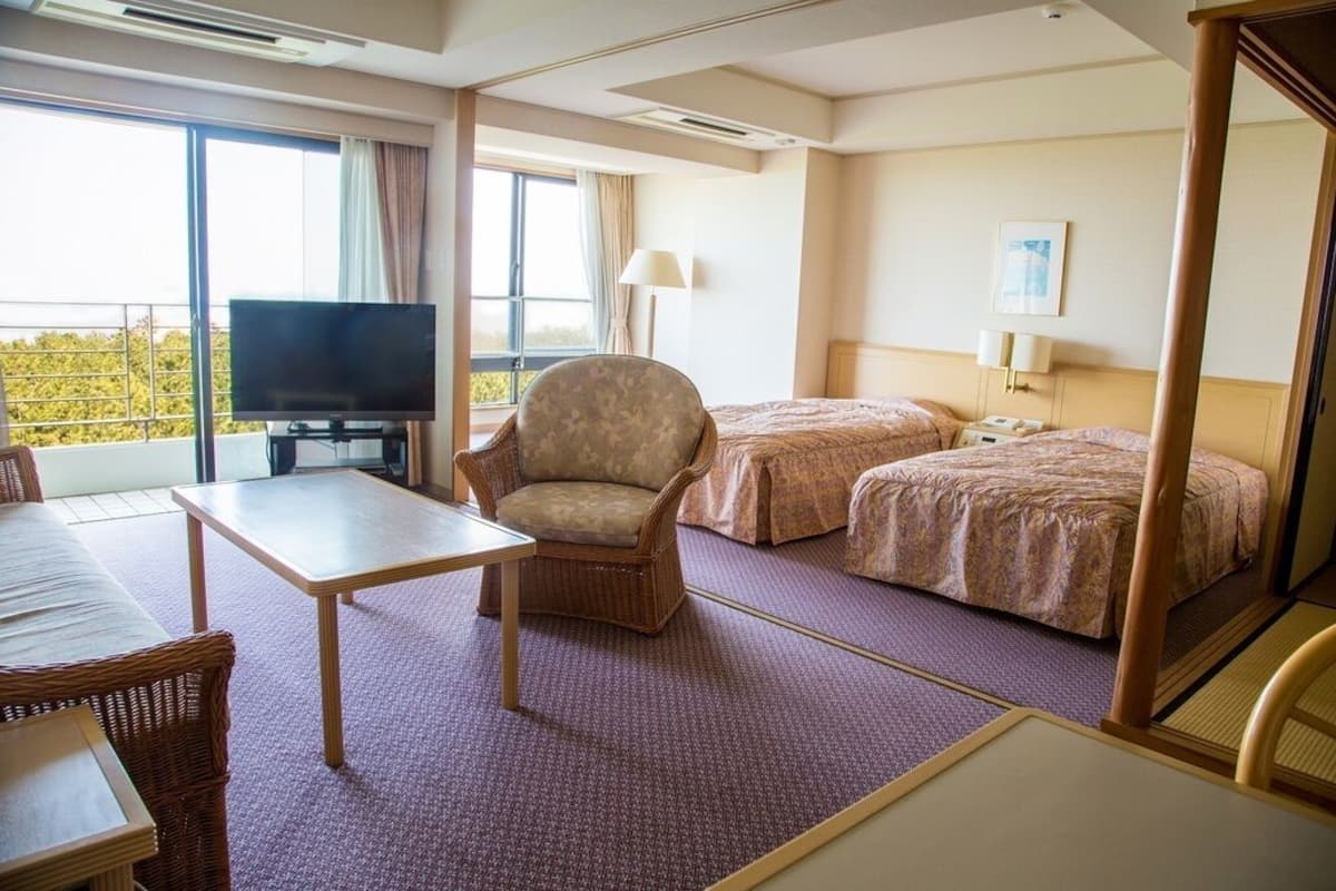 Une chambre d’hôtel équipée d’une télévision, de deux lits, d’une chaise, d’une table et d’un balcon avec vue.