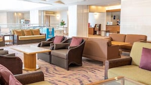 A spacious hotel lobby with multiple seating areas, a reception desk, and a large window providing a view of the outside. - Cottage Himuka (Miyazaki)