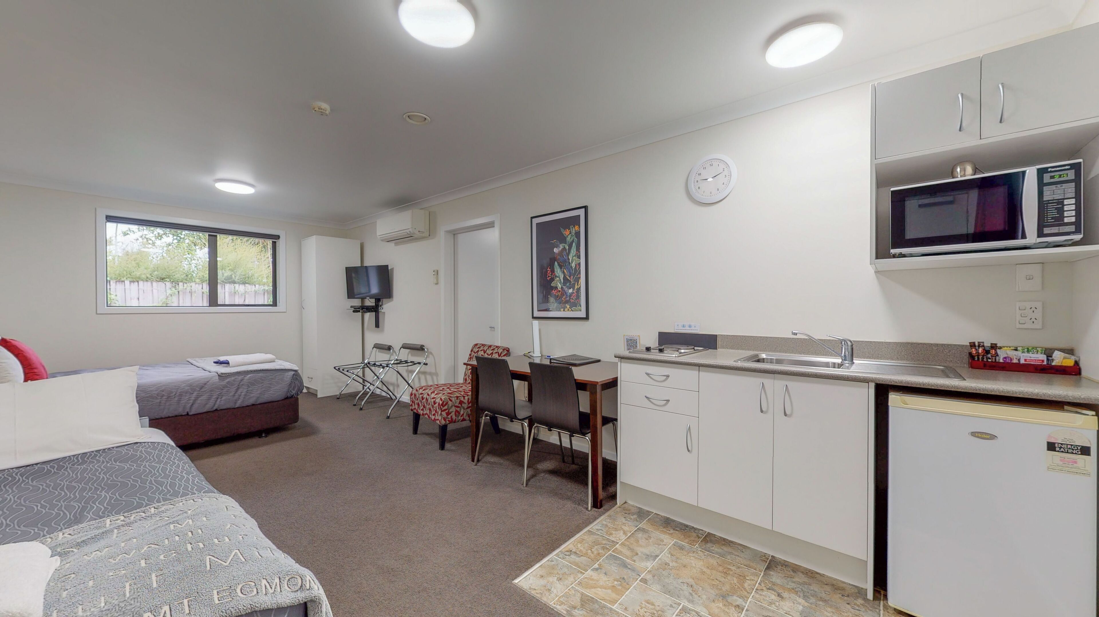 Habitación de hotel compacta con kitchenette, cama, televisor y zona de comedor.