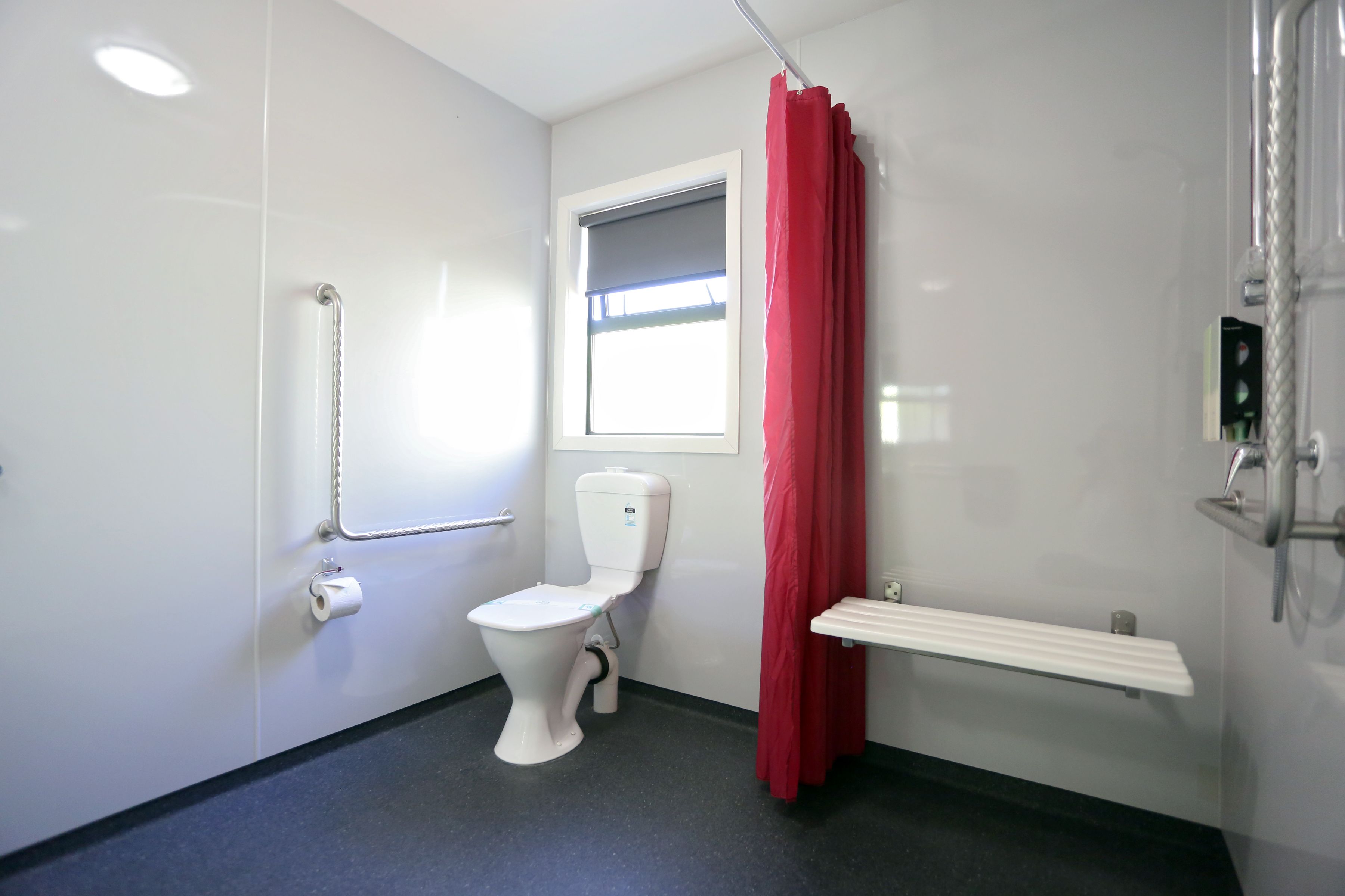 A bathroom with a toilet, a shower, a window, and a red curtain.