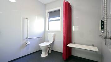 A bathroom with a toilet, a shower, a window, and a red curtain.