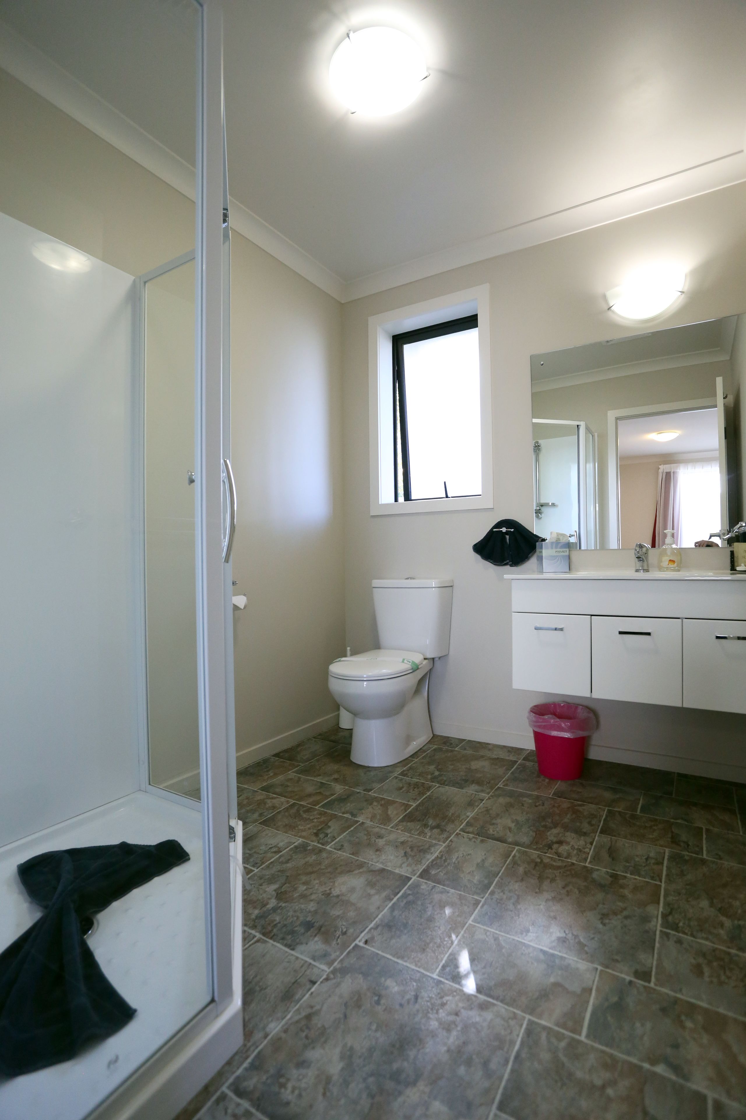 Un baño con mampara de vidrio, inodoro, lavamanos con espejo y ventana.