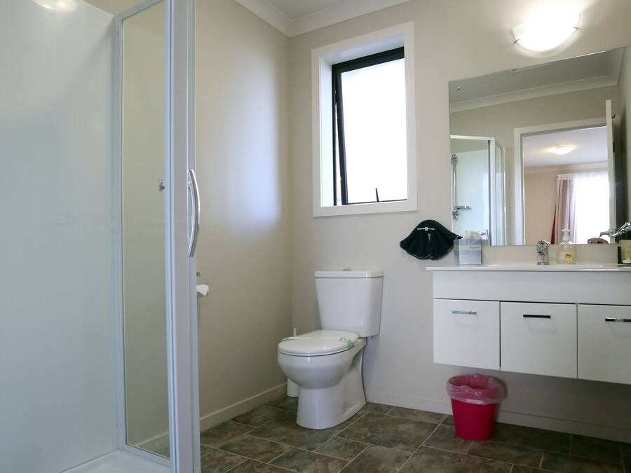 Un baño con mampara de vidrio, inodoro, lavamanos con espejo y ventana.