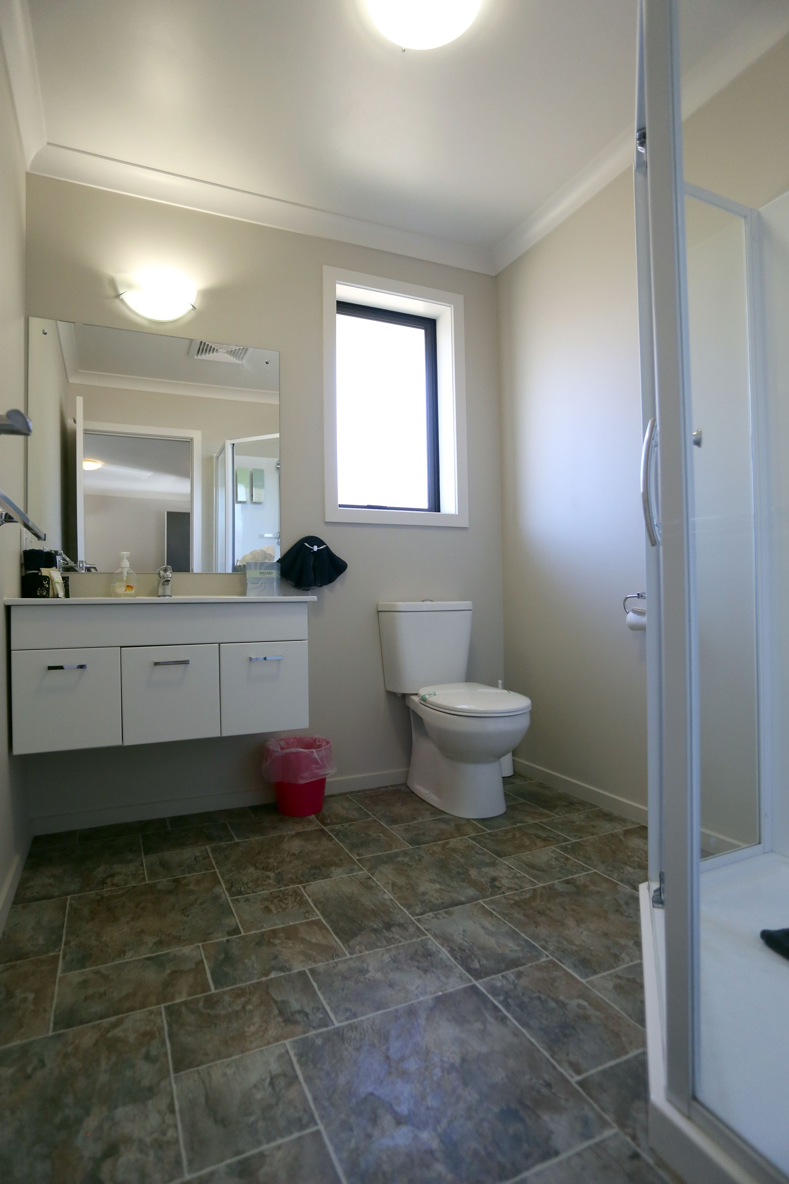 A bathroom with a white toilet, a sink with a mirror, a window, and a shower area.
