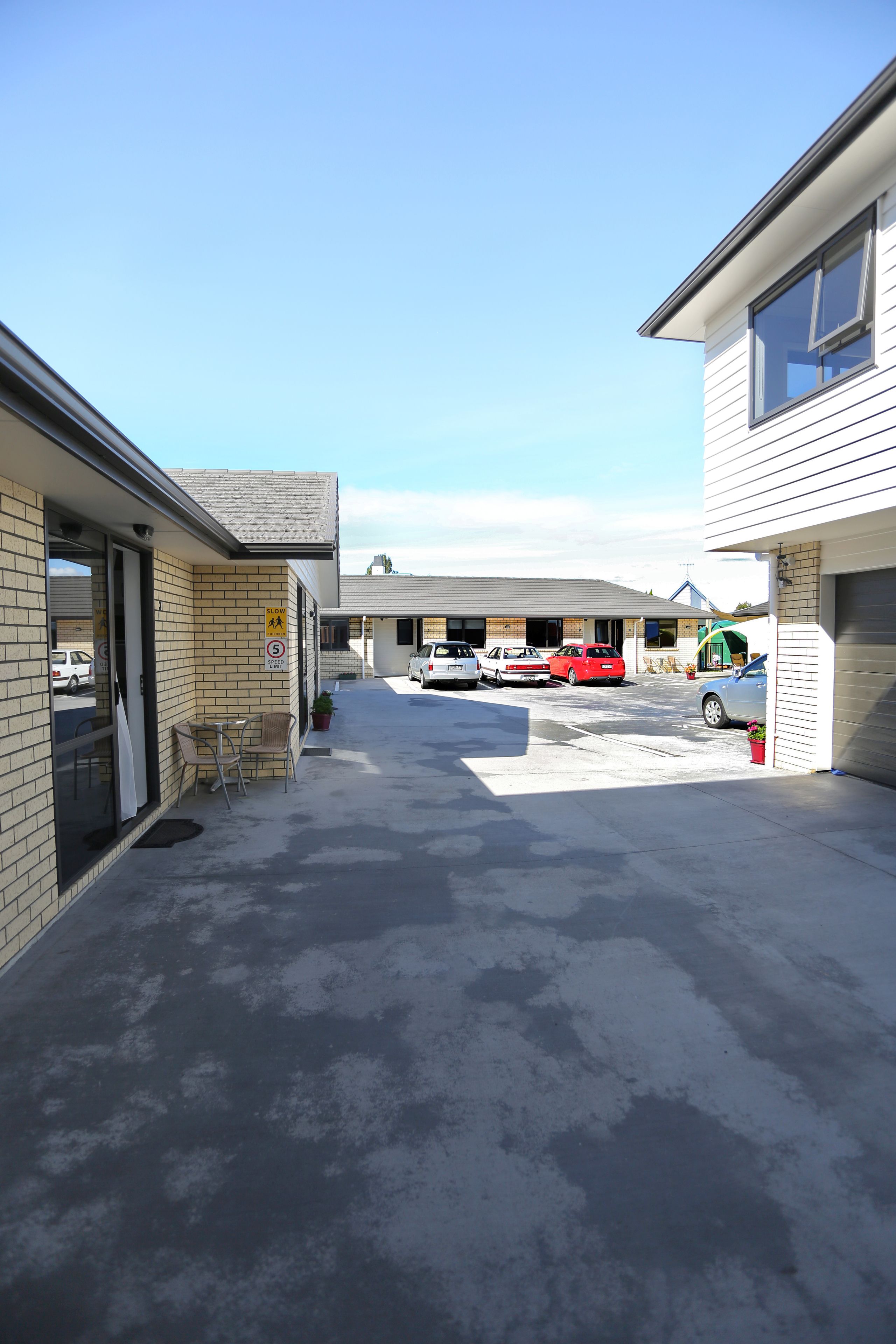 A parking area with several cars, a building with a garage, and a small outdoor seating area.