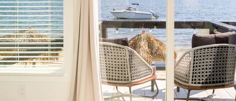 A room with a large window overlooking a body of water, featuring two wicker chairs and a table.