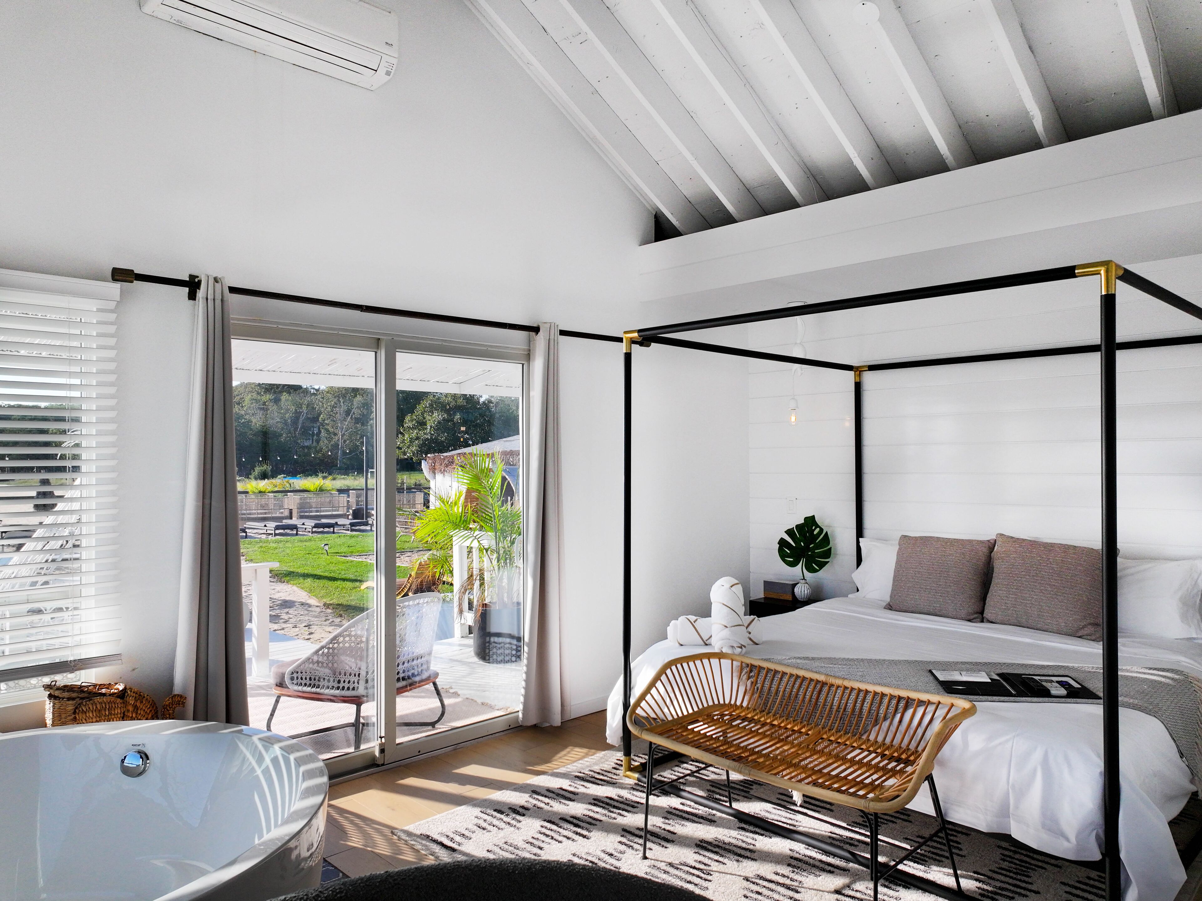A modern bedroom with a four-poster bed, a large window, and a view of the outdoors.