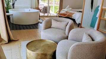 A modern bathroom with a freestanding bathtub, a large round mirror, and a seating area with a cushioned chair and ottoman.