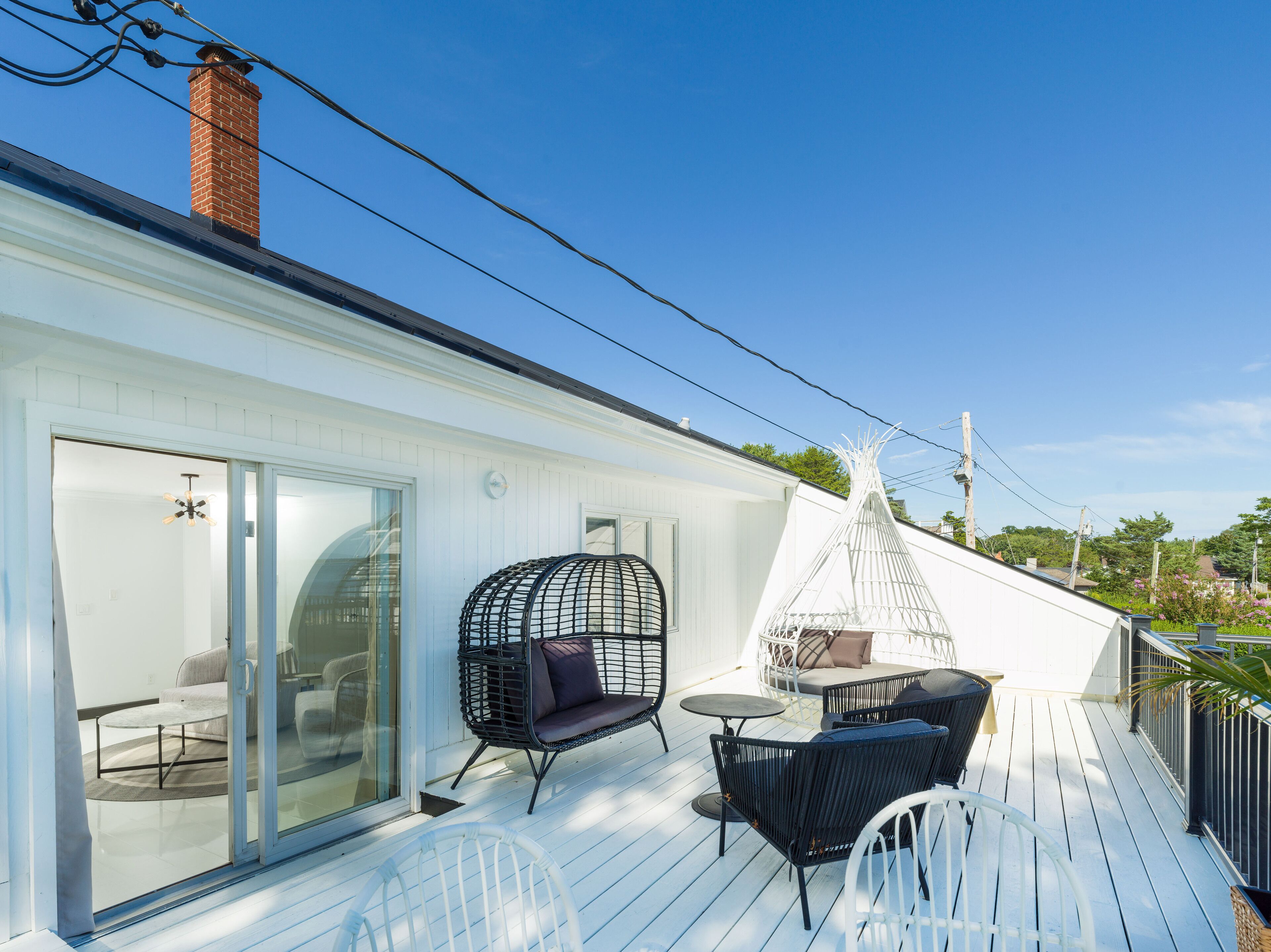 A covered outdoor deck with a glass door leading to a room, wicker furniture, and a white teepee-like structure.