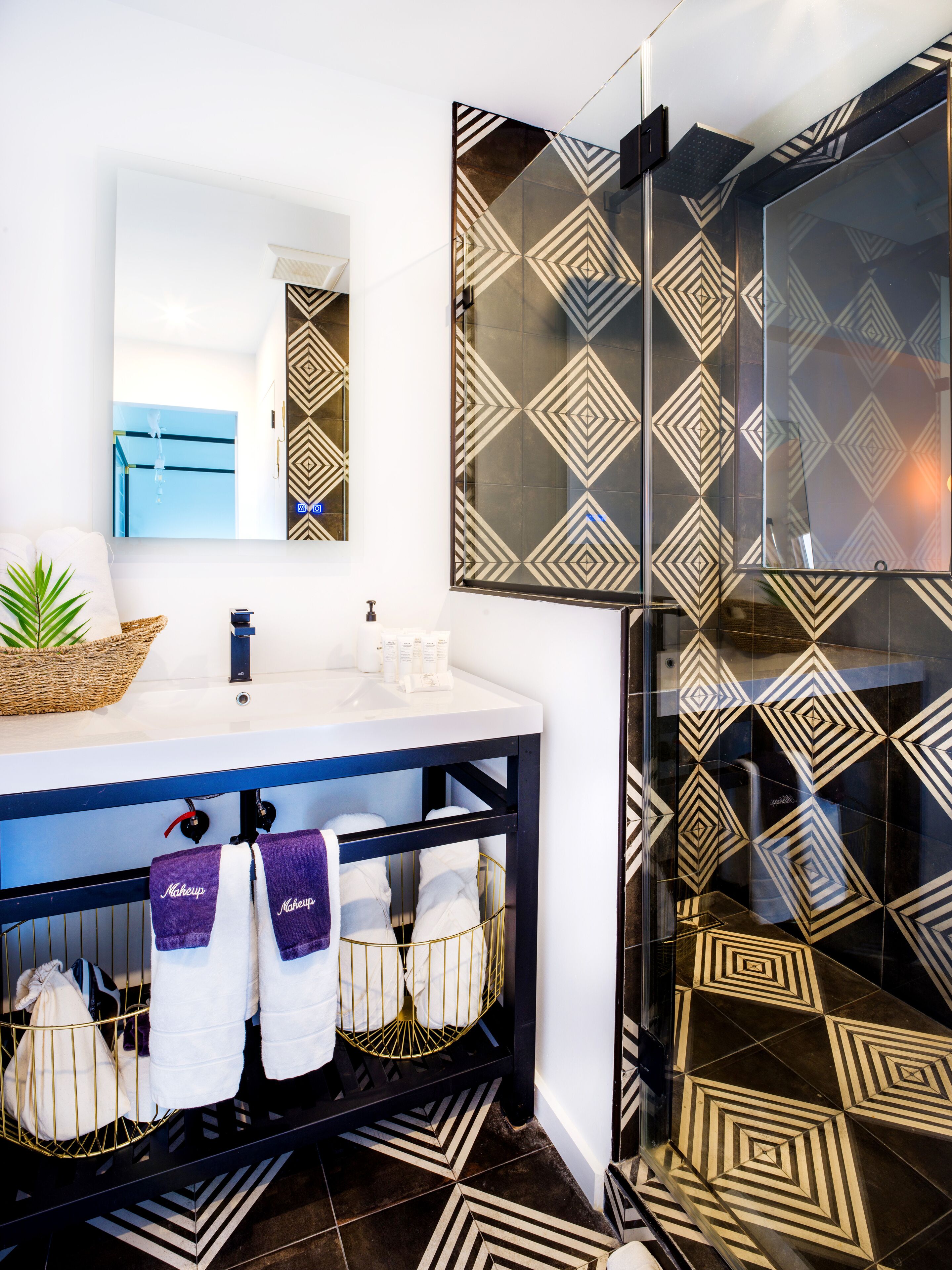 A modern bathroom with a large mirror, a sink with a blue countertop, and a shower with patterned tiles.