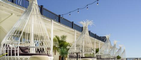 Outdoor seating areas with white wicker furniture and a clear blue sky.