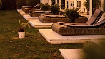 A covered outdoor seating area with lounge chairs and potted plants.