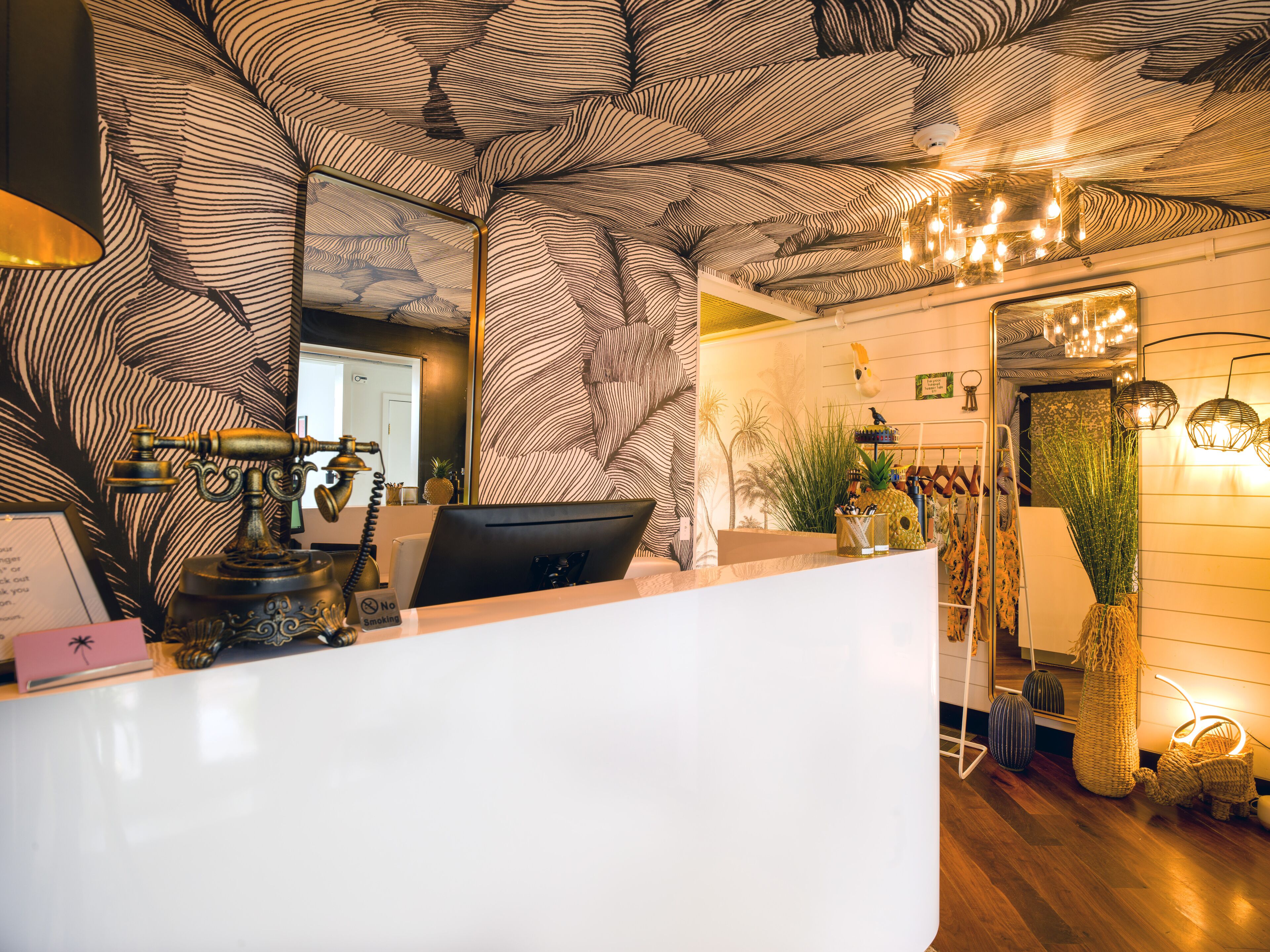 Un espace d’accueil doté d’un plafond orné de motifs, d’un bureau avec un ordinateur et de divers objets décoratifs, notamment un ananas et une plante.