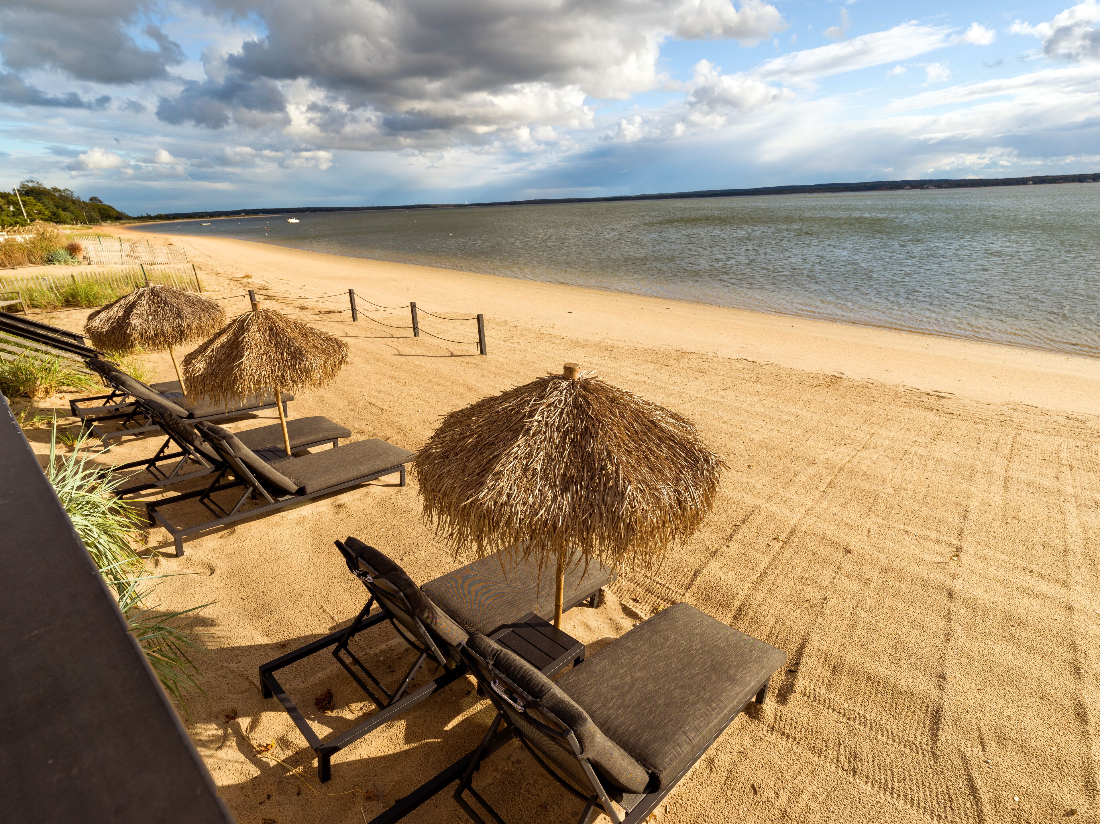 A beach with lounge chairs and thatched umbrellas.