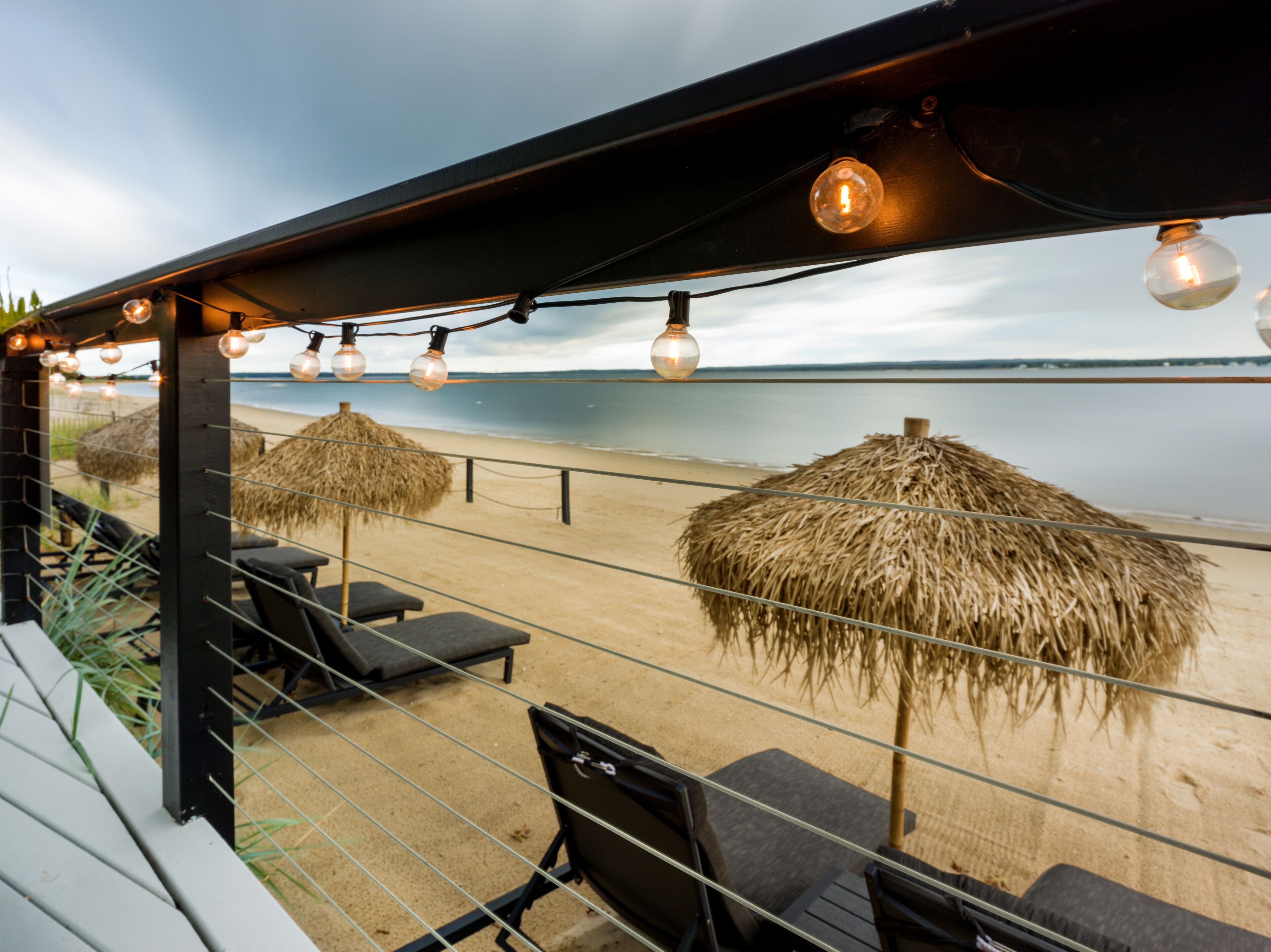 Ein Sitzbereich am Strand mit Reetdachschirmen und Liegestühlen mit Blick auf das Meer.