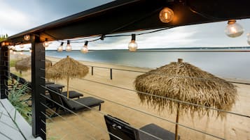 A beachside seating area with thatched umbrellas and lounge chairs, overlooking the sea.