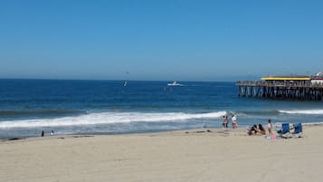 A beach with a pier extending into the ocean, a few people on the sand, and a boat in the water.