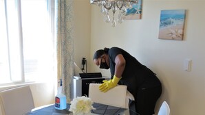 Una persona limpiando un comedor de vidrio con posavasos y un jarrón de flores.