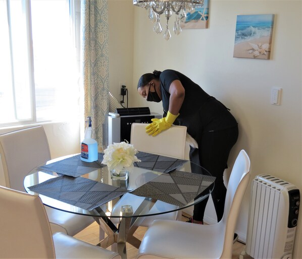 A person cleaning a glass-top dining table with placemats and a vase of flowers.
