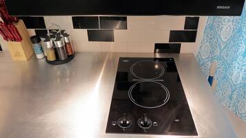A kitchen with a black induction cooktop, a stainless steel countertop, and a black range hood.