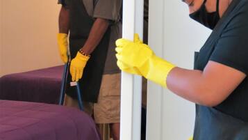 Two individuals cleaning a room, one mopping the floor and the other wiping a door handle.