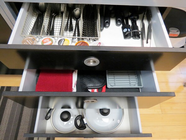A kitchen drawer with utensils, a red cloth, and pots.