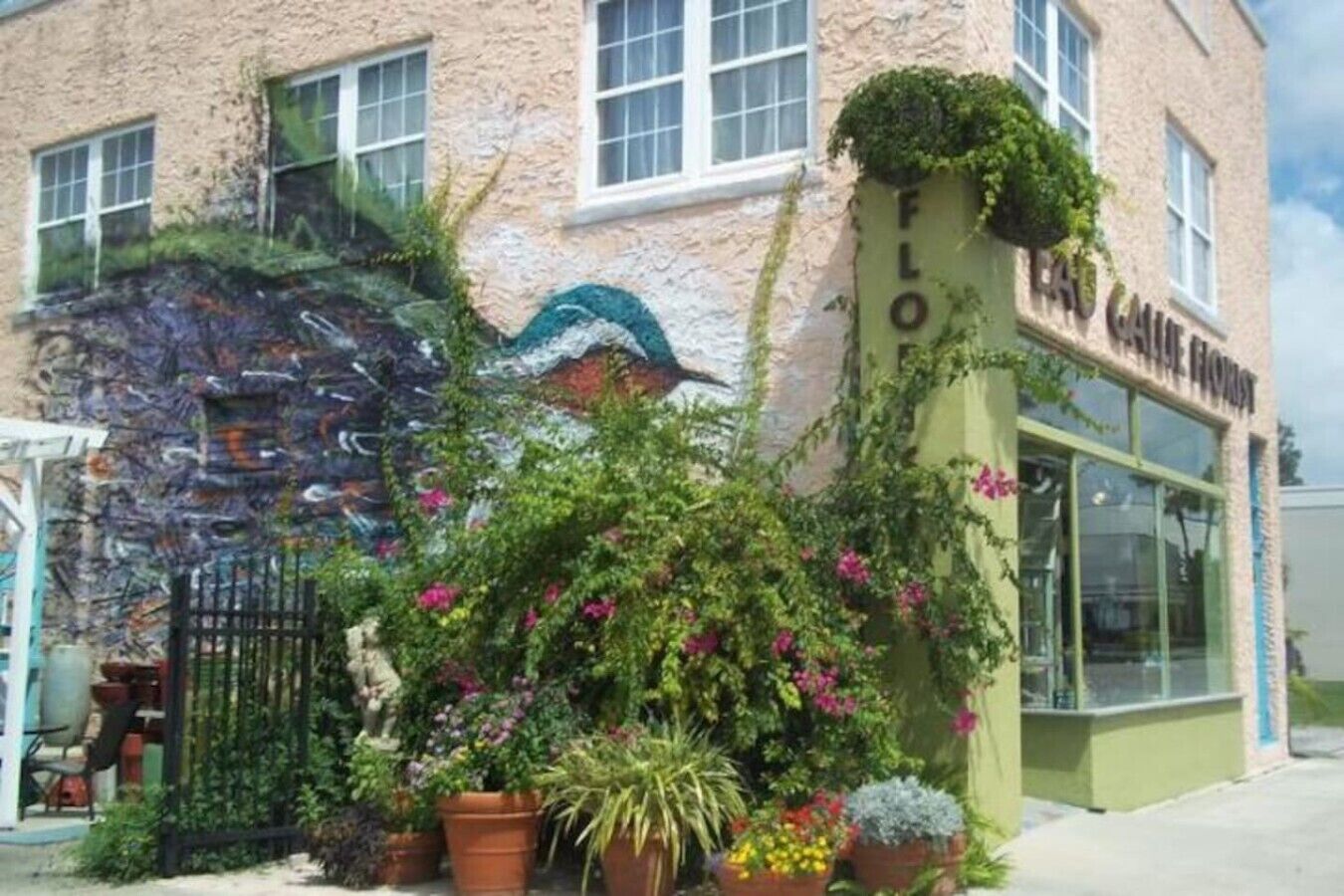 Un edificio con fachada verde, un cartel que dice 'FLOF' y diversas plantas en macetas al frente.