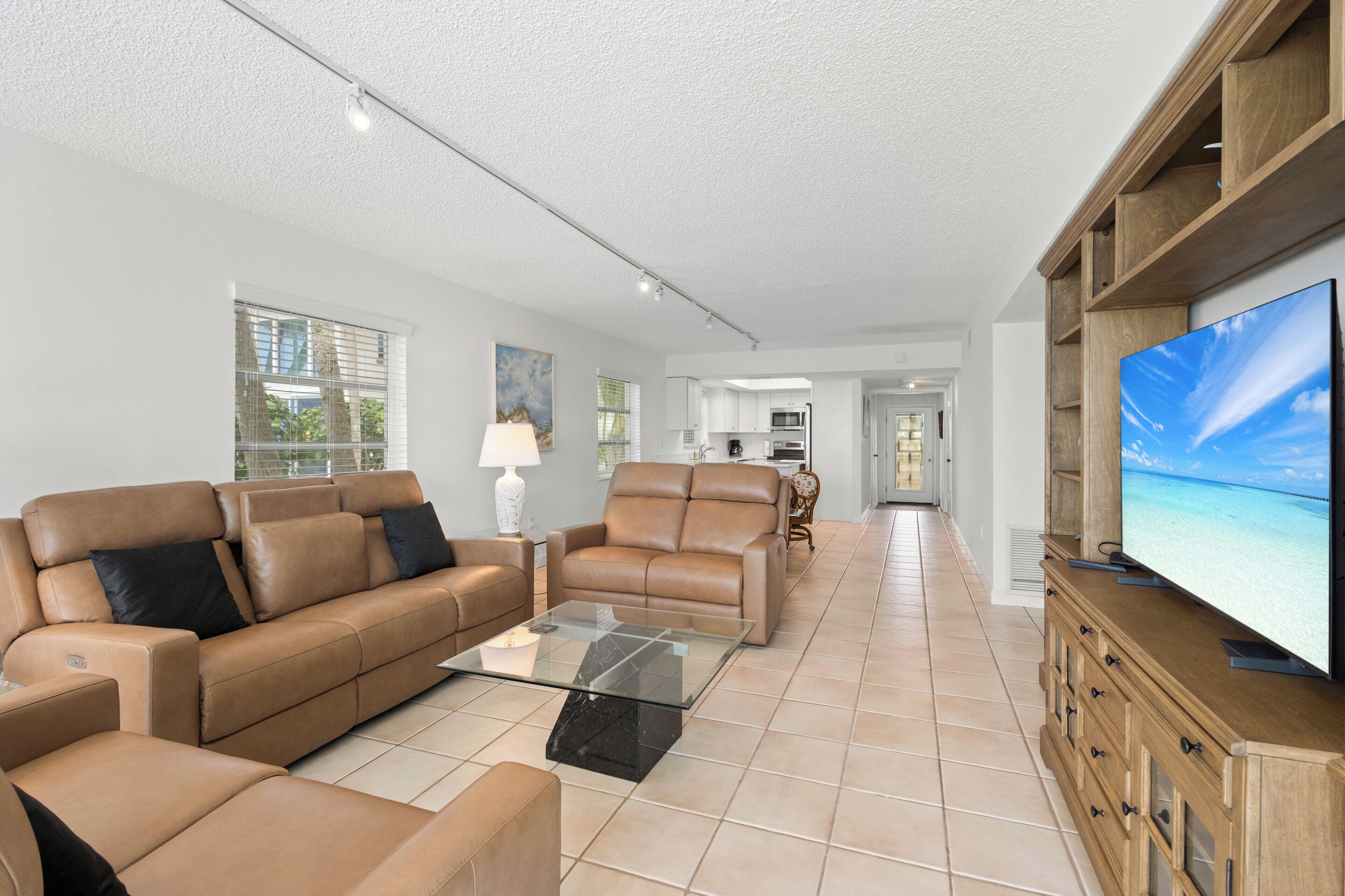 A spacious living room with a sofa, a glass coffee table, and a TV on a wooden cabinet.