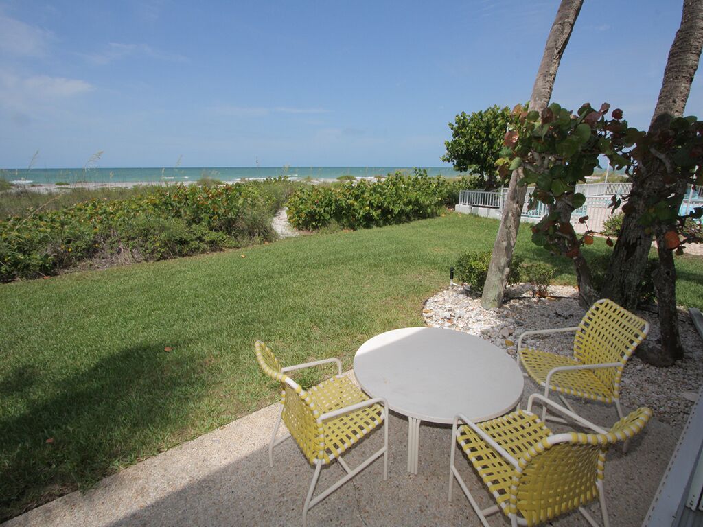 Une terrasse avec une table ronde et quatre chaises jaunes, donnant sur une plage avec une vue dégagée sur l’océan.