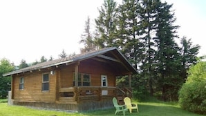 A wooden cabin with a porch, surrounded by trees. - Cajun Cedar Log Cottages 2 Bdrm -  Unit 2 (Margaree Forks Cape Breton)