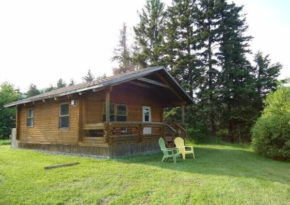 Une cabane en bois avec un porche, entourée d’arbres.