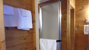 A wooden cabin bathroom with a glass shower door, wooden walls, and towels hanging on the wall. - Cajun Cedar Log Cottages 2 Bdrm -  Unit 2 (Margaree Forks Cape Breton)