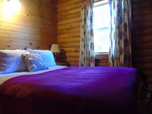 Une chambre aménagée dans un chalet en rondins, avec un lit, des rideaux à motifs floraux et une fenêtre.