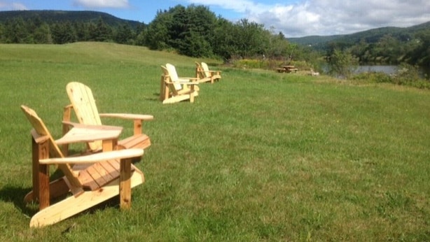 A grassy field with wooden Adirondack chairs and a picnic table. - Cajun Cedar Log Cottages 2 Bdrm -  Unit 2 (Margaree Forks Cape Breton)