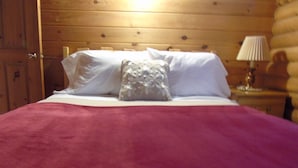 A bed with a red blanket and a decorative pillow in a wooden room. - Cajun Cedar Log Cottages 2 Bdrm -  Unit 2 (Margaree Forks Cape Breton)