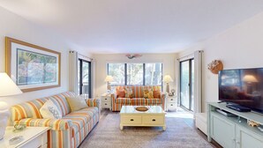 A living room with striped sofas, a glass coffee table, a television, and a painting on the wall.