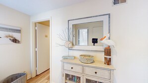 A hallway with a white door marked '68', a small wicker basket, a decorative bowl, a mirror with a wooden frame, and a white pelican sculpture.