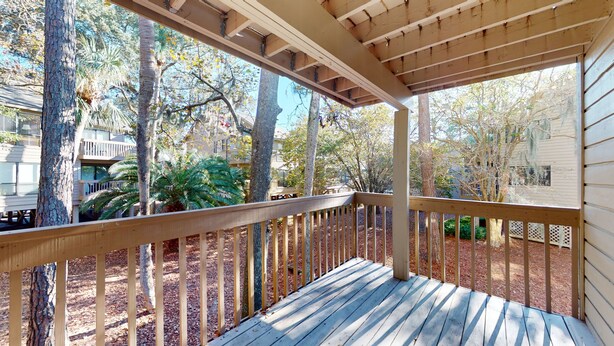 A wooden deck with a railing, surrounded by trees and a building.