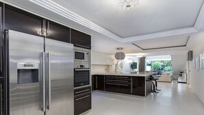 Une cuisine moderne dotée d’un grand réfrigérateur en acier inoxydable, d’un four encastré, d’un micro-ondes et de meubles de rangement aux couleurs sombres.