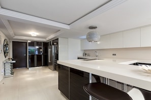 A modern kitchen with a large island, stainless steel appliances, and a decorative crystal pendant light.