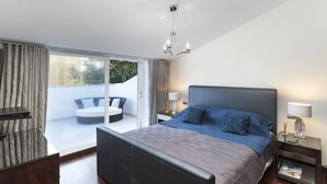 Une chambre moderne avec un grand lit, un balcon doté d’un coin salon et un lustre.