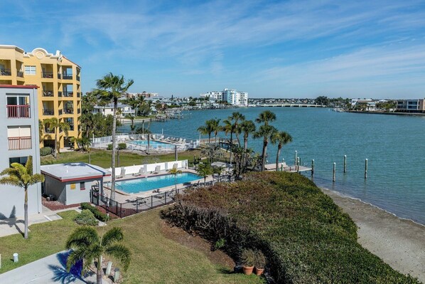 A waterfront hotel with a pool, palm trees, and a view of the water.