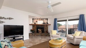 Ein Wohnzimmer mit Flachbildfernseher, Rattanmöbel, Kamin und Balkon mit blauen Vorhängen.