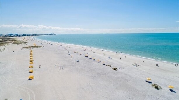Ein Strand mit Reihen gelber Sonnenschirme und freiem Blick auf das Meer.