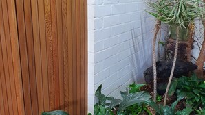 A wooden fence, a white brick wall, and a potted plant with green leaves. - BANNISTER COVE MOLLYMOOK - Art House - spa - (Mollymook Beach)