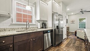 A modern kitchen with dark wood cabinets, stainless steel appliances, a granite countertop, and a window with blinds. - Shore Beats Work, Modern 3 Bedroom Vacation Home w/ Community Pool & Clubhouse (Kill Devil Hills)